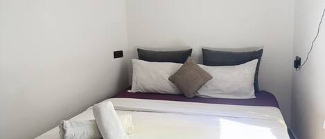 A single bed with a wooden frame, white bedding, and two pillows.