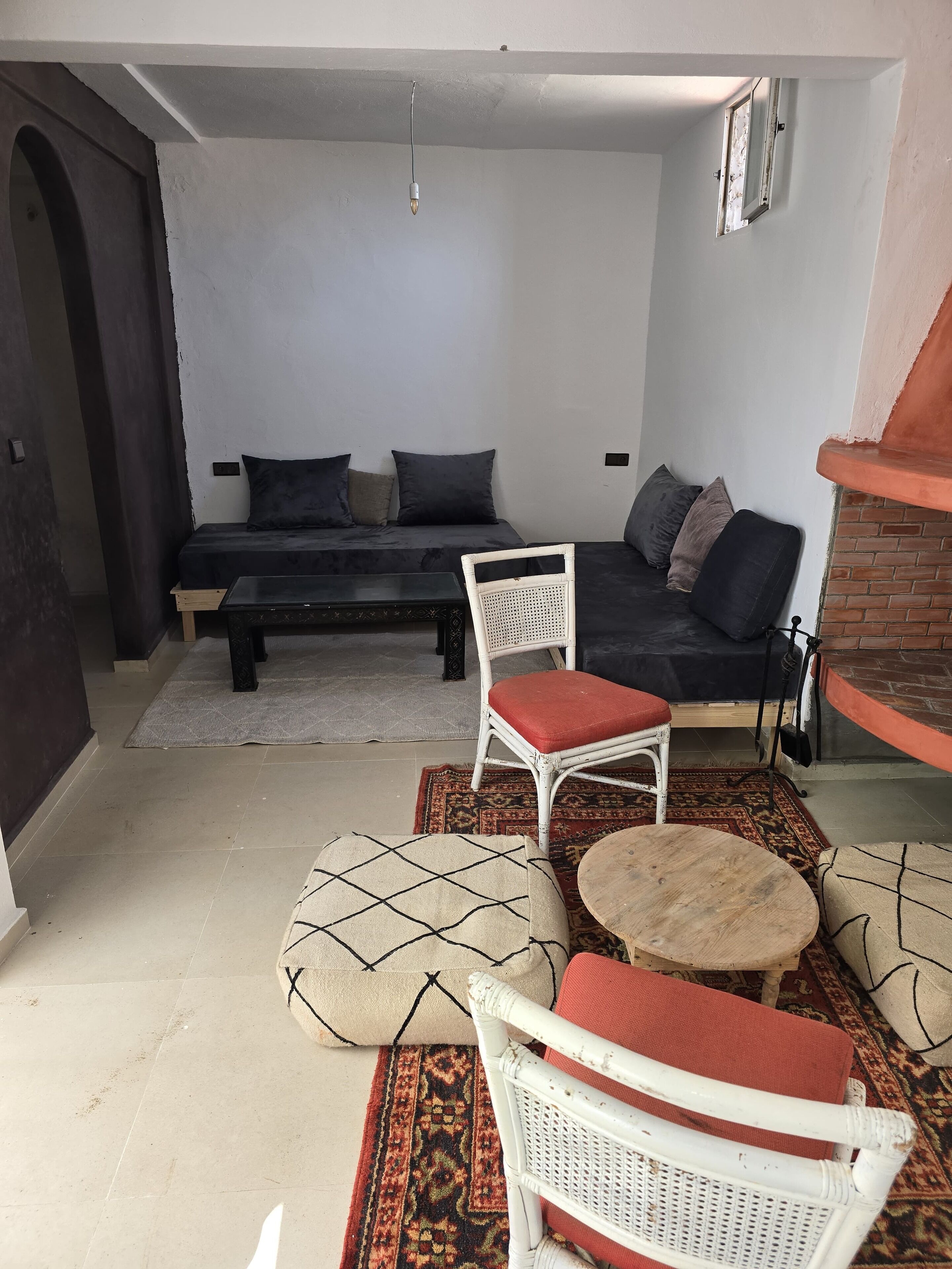 Uma sala de estar aconchegante com um sofá, duas poltronas de vime branco, uma mesa de centro pequena e um tapete estampado.