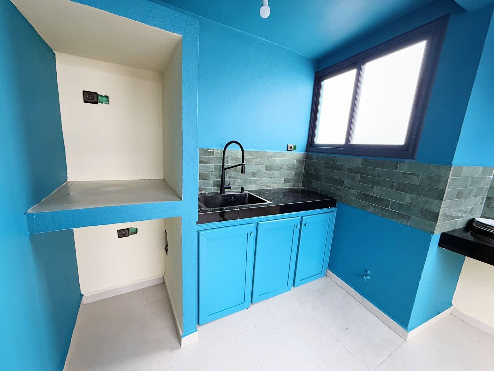 A kitchen with blue cabinets, a black countertop, and a window.