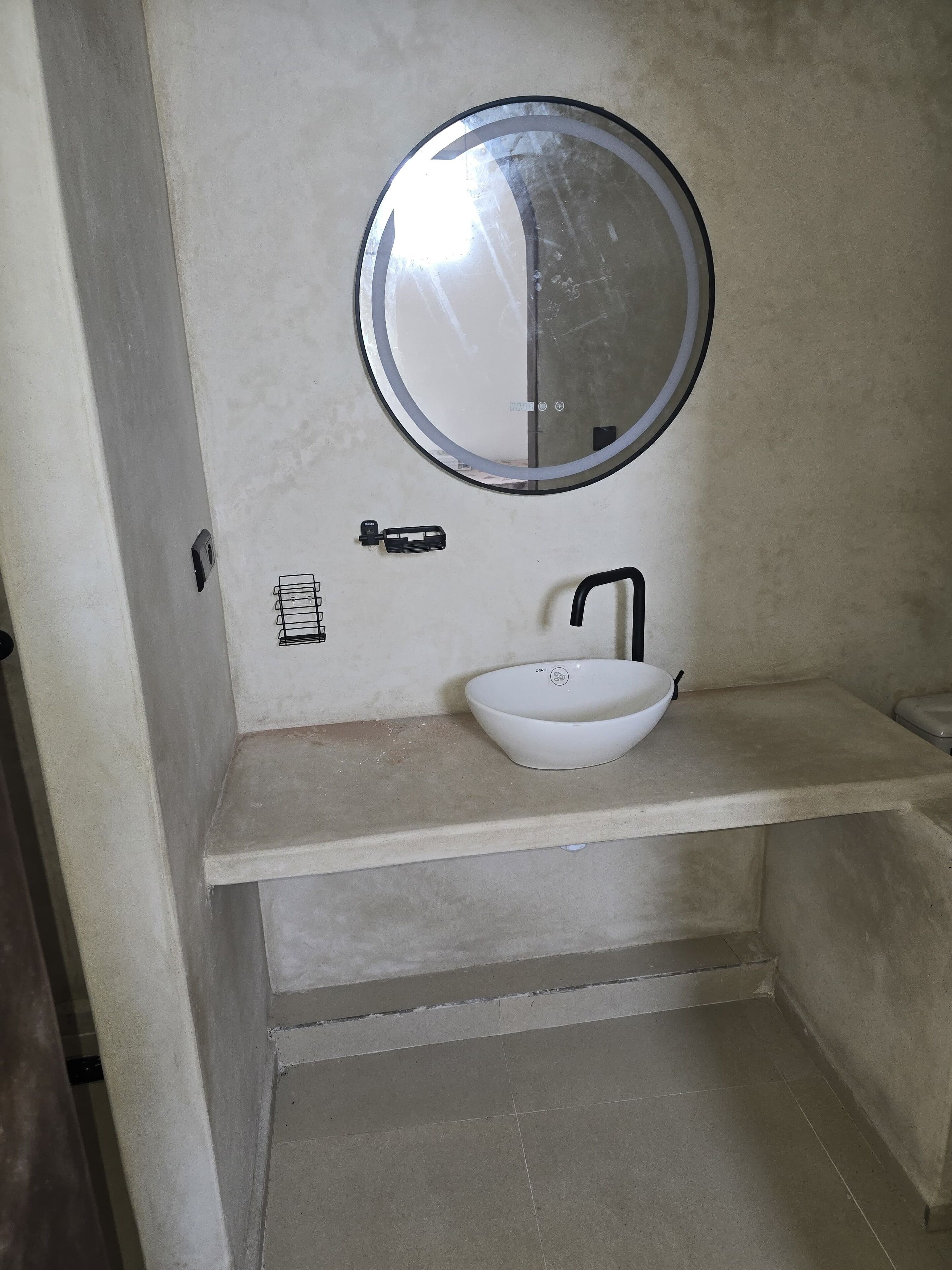 Un baño con un espejo redondo, un lavamanos blanco y un grifo negro.
