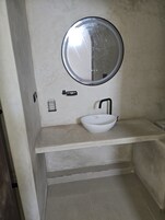 Un baño con un espejo redondo, un lavamanos blanco y un grifo negro.