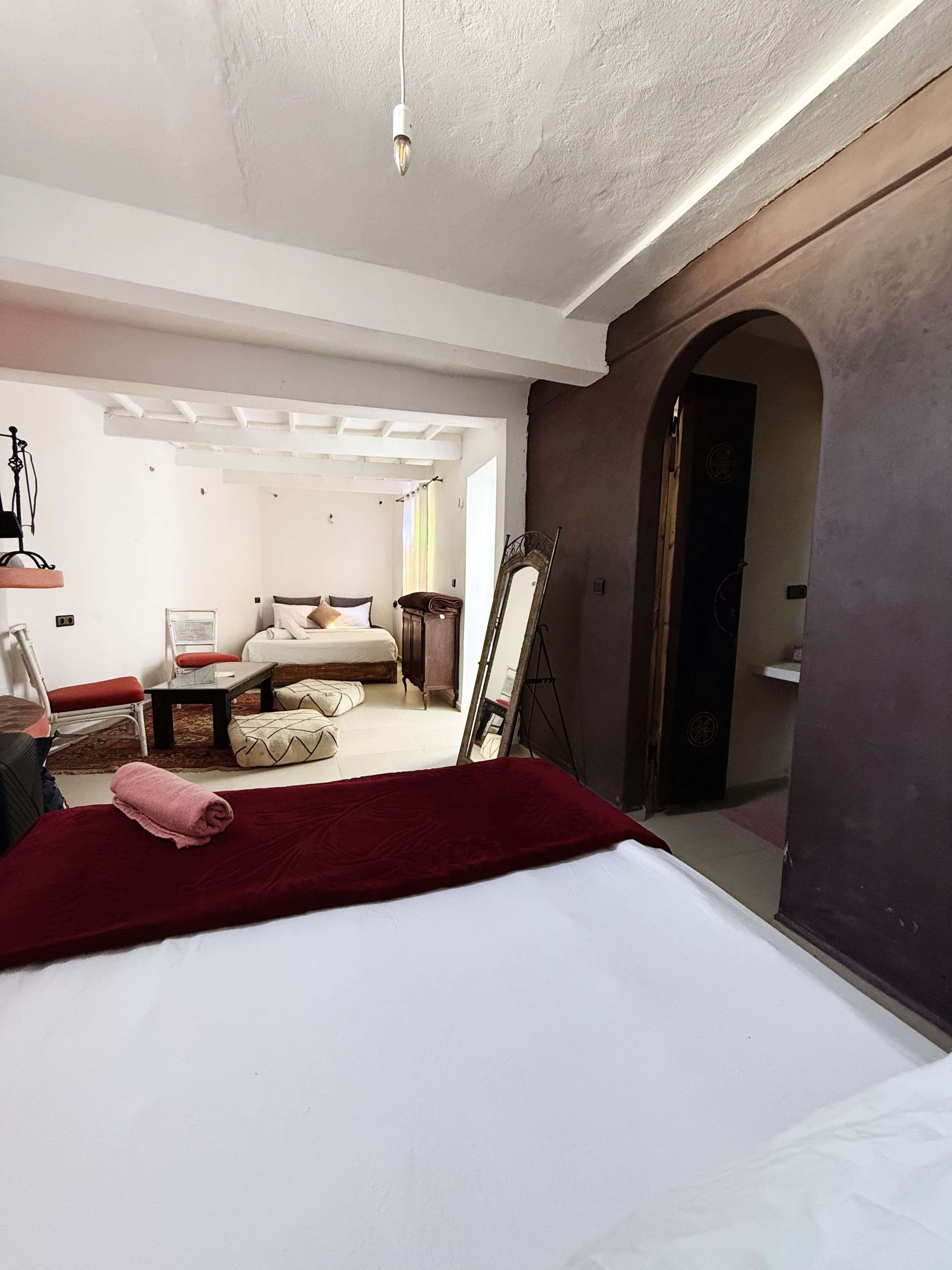 A hotel room with a bed, a sitting area with a table and chairs, a mirror, and a view of another room through an archway.
