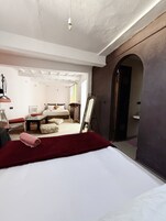 Una camera d'hotel con un letto, un angolo salotto con tavolo e sedie, uno specchio e vista su un'altra stanza attraverso un arco.