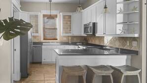 A kitchen with white cabinets, a central island with stools, a microwave, and a window with blinds.