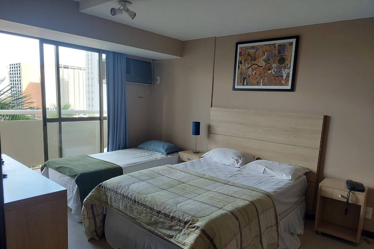 A hotel room with two beds, a ceiling fan, a window with curtains, a wall-mounted TV, and a framed abstract painting.