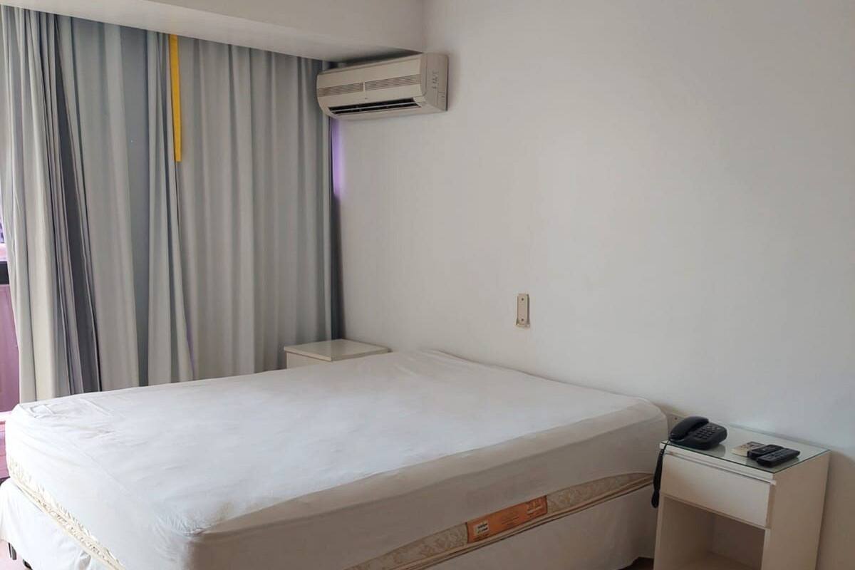 A hotel room with a large bed, a bedside table with a phone, and an air conditioning unit on the wall.
