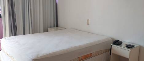 Una habitación de hotel con una cama grande, una mesita de noche con teléfono y un equipo de aire acondicionado en la pared.