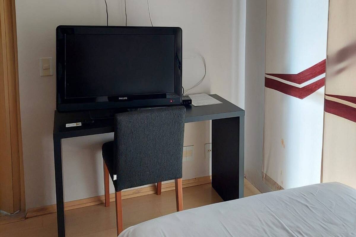 A hotel room with a bed, a desk with a television, and a chair.