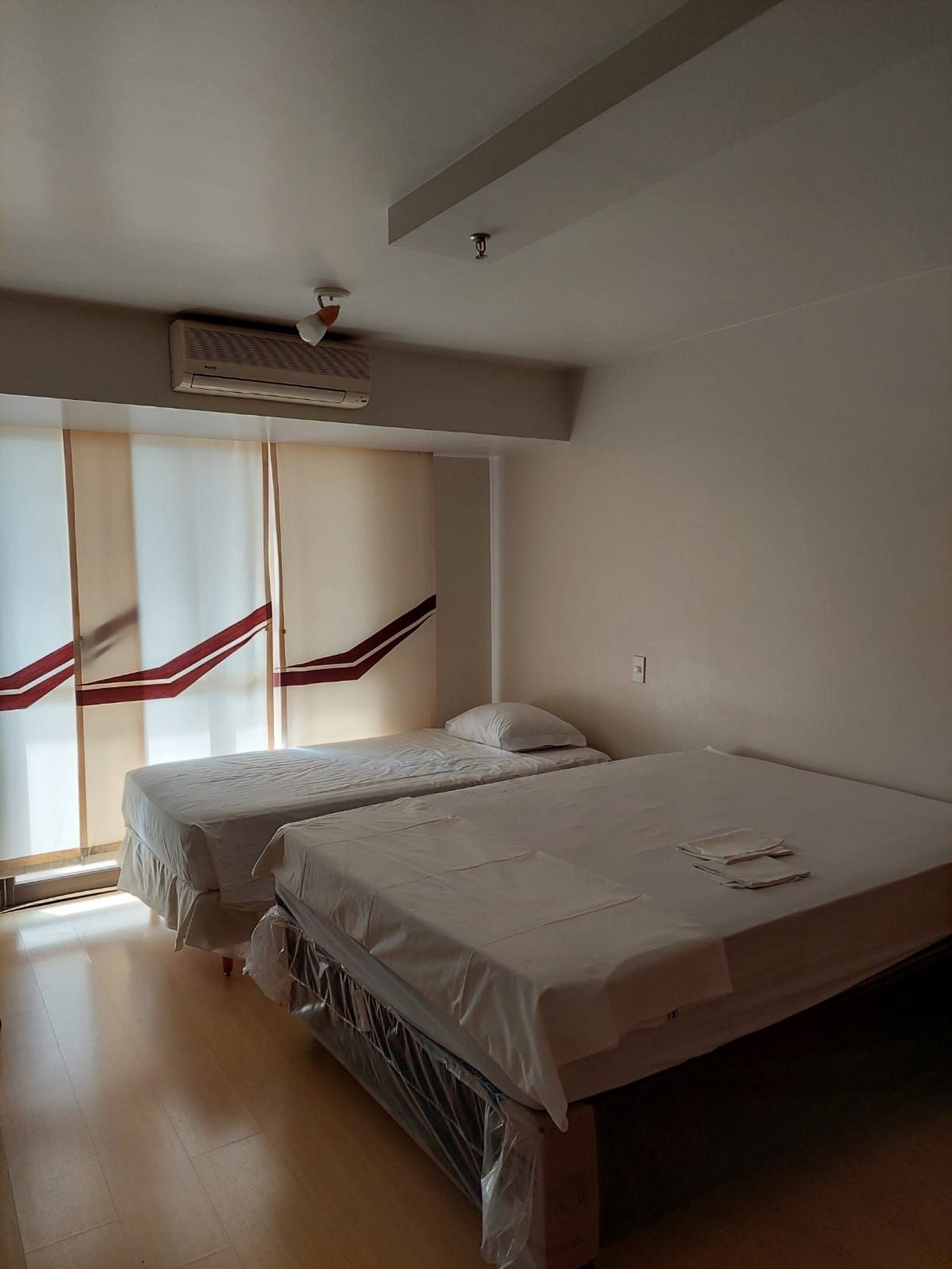 Una habitación con dos camas, ventilador de techo y ventana con persianas.