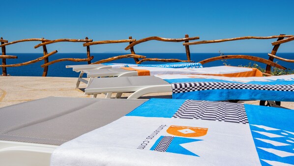Eine Strandlounge mit Liegestühlen und Tischen, einer Holzlattenumzäunung und Meerblick.