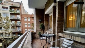 Ein Balkon mit zwei Metallstühlen und einem kleinen Tisch, mit Blick auf einen Innenhof mit Gebäuden.