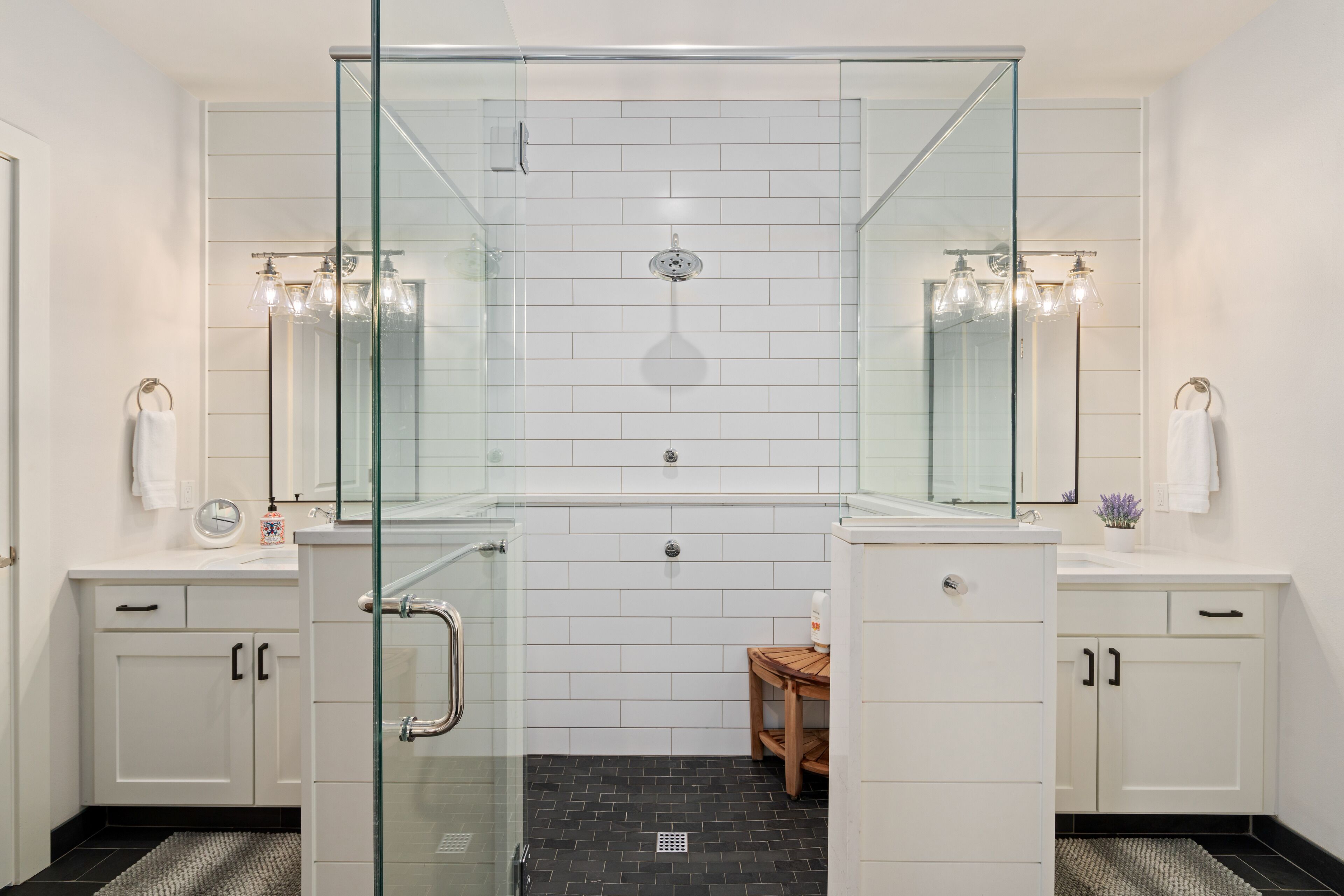 A modern bathroom with a glass-enclosed shower, white tiled walls, and dual sinks with mirrors.