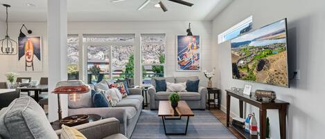 A spacious living room with a large TV, comfortable seating, and a ceiling fan.