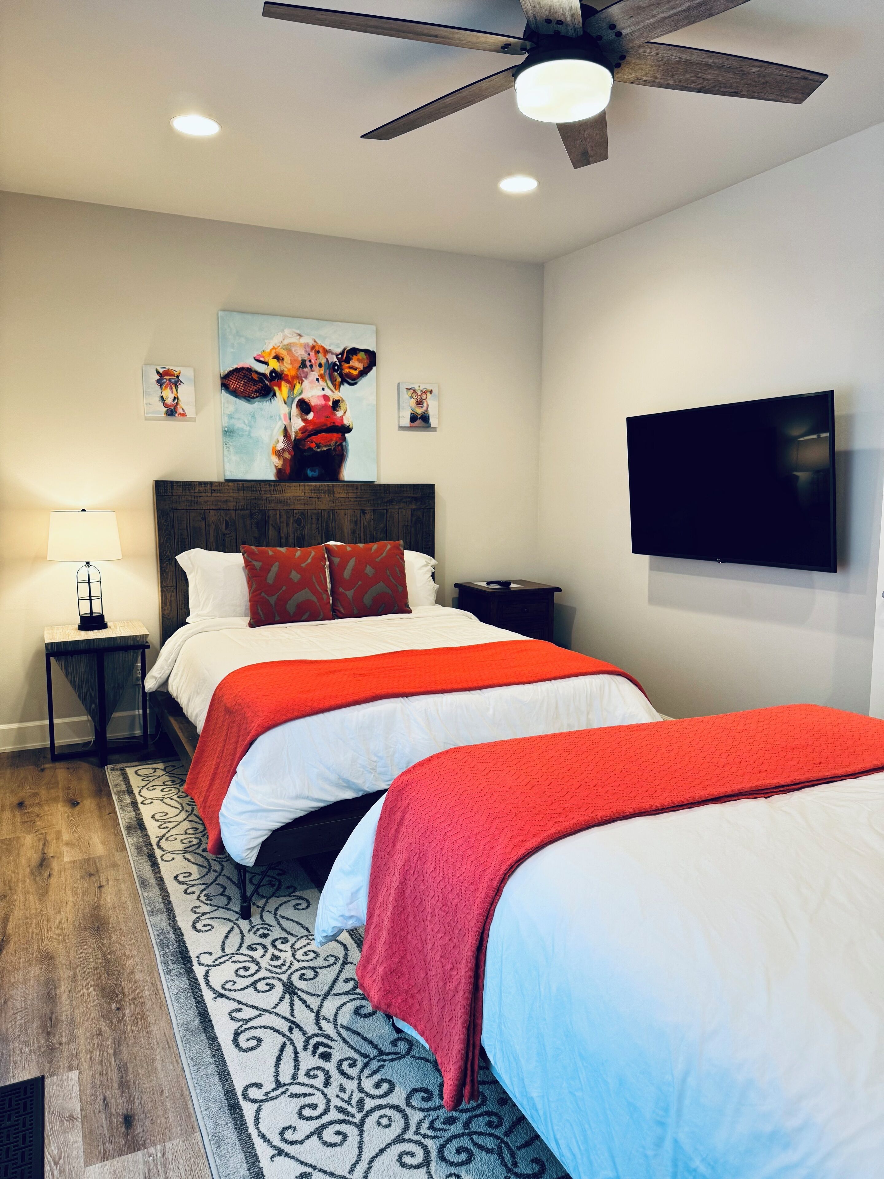 A bedroom with two beds, a ceiling fan, a TV, and artwork on the wall.