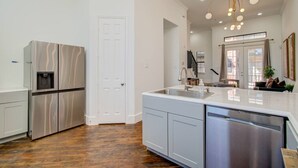 A modern kitchen with stainless steel appliances, a large island with a sink, and a wooden floor. - Chic Med Center Condo with Secure Parking (Houston)