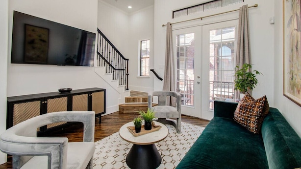 A spacious living room with a staircase, a large TV, and a green sofa. - Chic Med Center Condo with Secure Parking (Houston)