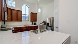 A modern kitchen with a large island, wooden cabinets, stainless steel appliances, and a view of the outdoors. - Chic Med Center Condo with Secure Parking (Houston)