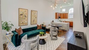 A modern living room with a teal sofa, a grey armchair, and a coffee table. There are two framed butterfly artworks on the wall. - Chic Med Center Condo with Secure Parking (Houston)