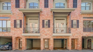 A multi-story residential building with brick facades, multiple balconies, and garage doors. - Chic Med Center Condo with Secure Parking (Houston)