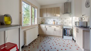 A kitchen with a window, a radiator, a microwave, and a red stool.