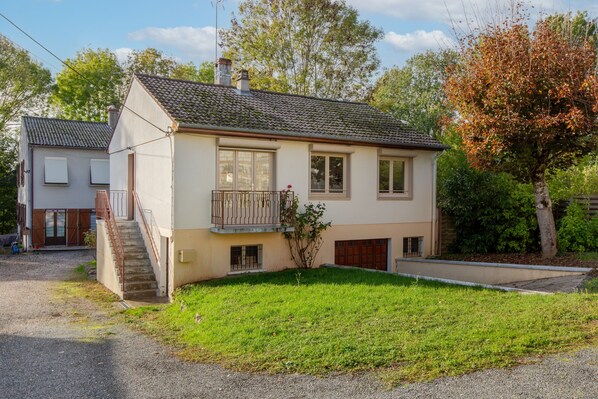 Une maison à deux étages avec un balcon, un jardin devant et un bâtiment voisin.