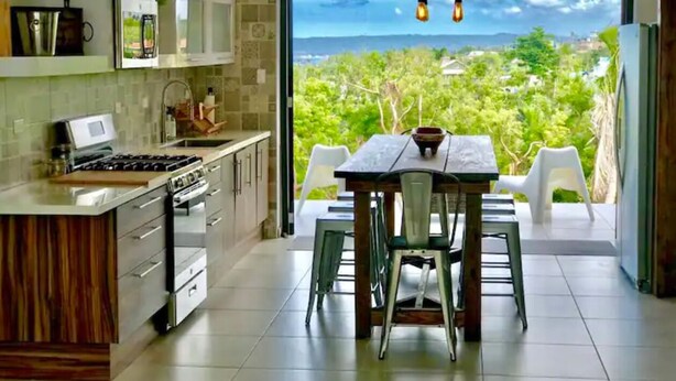 A modern kitchen with a dining area, large windows, and a view of greenery. - Minutes from the beach, modern home with ocean views. Pet friendly!   (Rincón)