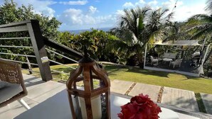 A patio with a white table, a lantern, a vase with red flowers, and a cup of coffee. - Minutes from the beach, modern home with ocean views. Pet friendly!   (Rincón)