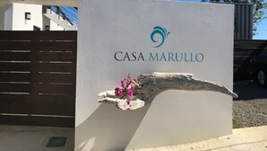 A sign for CASA MARULLO with a logo, a wooden branch with flowers, and a clear blue sky in the background. - Minutes from the beach, modern home with ocean views. Pet friendly!   (Rincón)