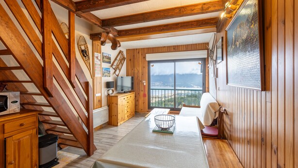 Un interior de madera con comedor, televisor y vistas al exterior.