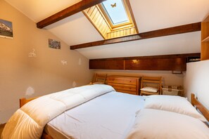 Ein Schlafzimmer mit Dachfenster, Holzbalken, einem Bett, einem Sessel und einem kleinen Tisch.