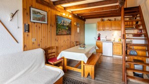 Una habitación acogedora con un banco de madera, una mesa y un sofá. Cuenta con una zona de cocina con armarios de madera y un lavamanos.