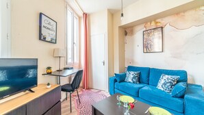 Un salon moderne avec un canapé bleu, un téléviseur à écran plat, un bureau et une table à manger préparée pour deux personnes.