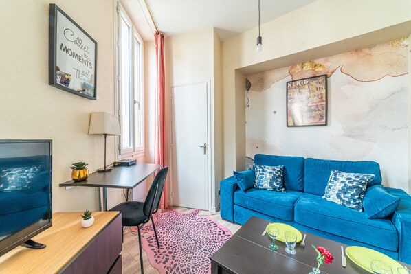 A living room with a blue sofa, a TV, a desk with a lamp, and a framed quote on the wall.