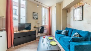 Un salon moderne avec un canapé bleu, une table à manger avec de l’assiette verte, un téléviseur et un coin cuisine avec un réfrigérateur.