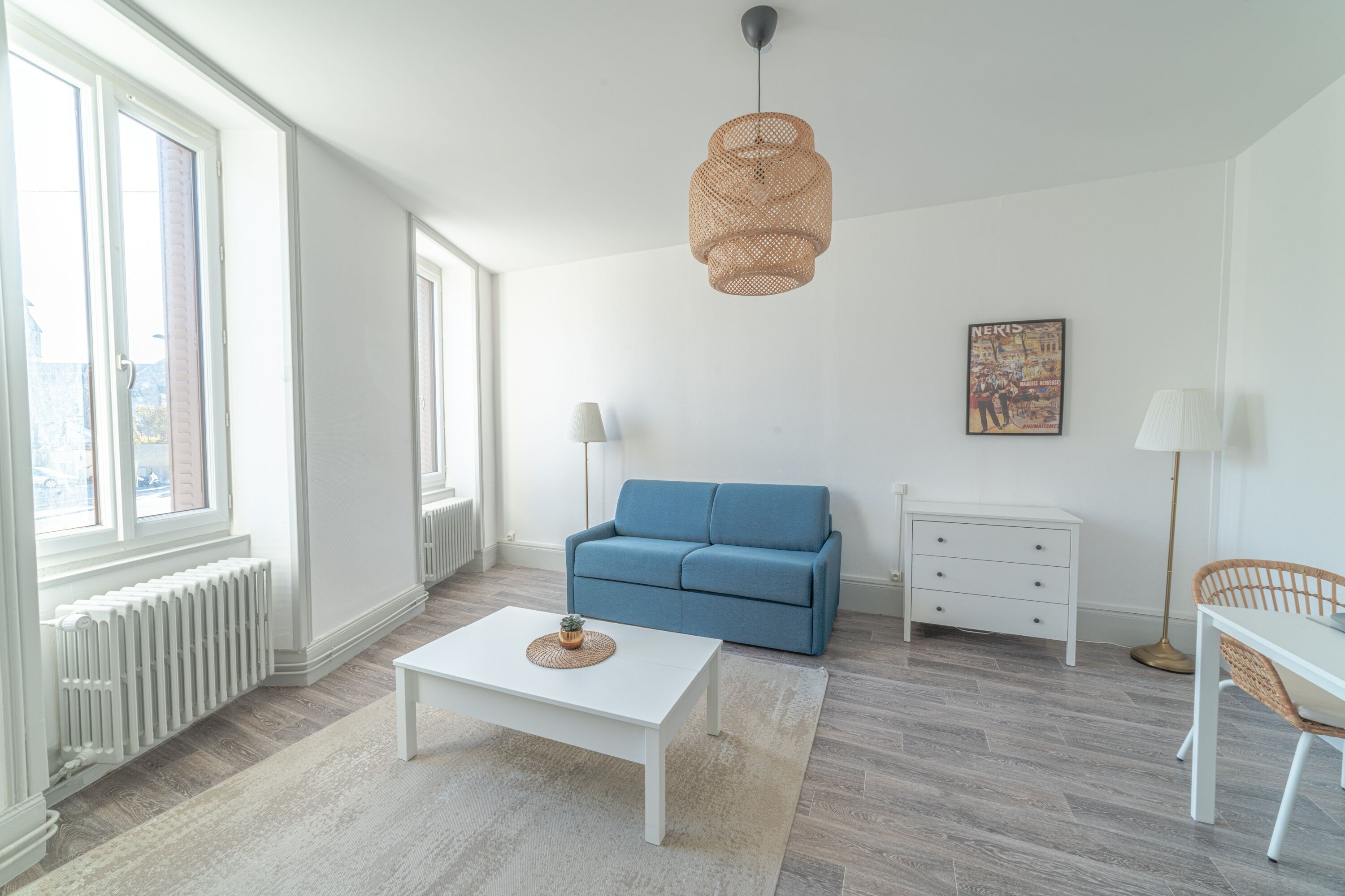 Een moderne woonkamer met een witte salontafel, een blauwe bank, een witte dressoir en een rieten stoel.