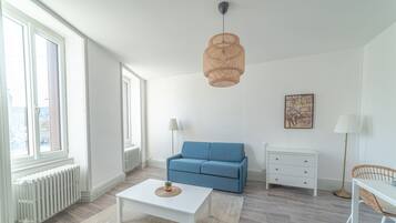 Een moderne woonkamer met een witte salontafel, een blauwe bank, een witte dressoir en een rieten stoel.