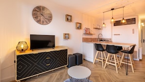 A modern living room with a TV, a clock, and a dining area with chairs and a table.