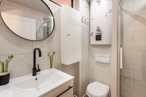 A modern bathroom with a white sink, black faucet, and a round mirror. There is a toilet and a glass shower enclosure.