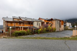 A row of multi-story buildings with balconies, a parking lot, and a mountainous backdrop.