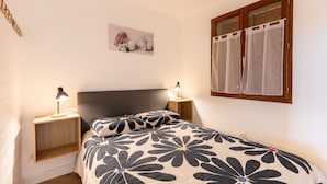 A bedroom with a bed, two bedside tables with lamps, a window with curtains, and a wall-mounted picture.