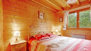 Ett sovrum i en stuga med träpanel, inrett med en säng, två sänglampor, ett nattduksbord och ett fönster med gardiner.