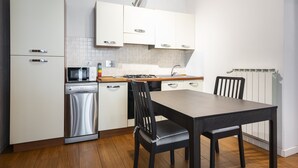 A modern kitchen with white cabinets, stainless steel appliances, a wooden dining table, and a black chair. - Berni - One Bedroom Apartment, Sleeps 2 (Florence)