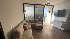 Un soggiorno moderno con un divano beige componibile, una TV a schermo piatto montata a parete e un balcone con vista sulla città.