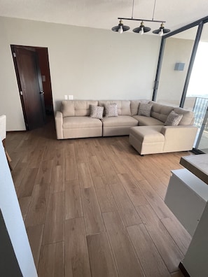 Un soggiorno moderno con un divano beige a forma di L, cuscini decorati e un pavimento in legno.