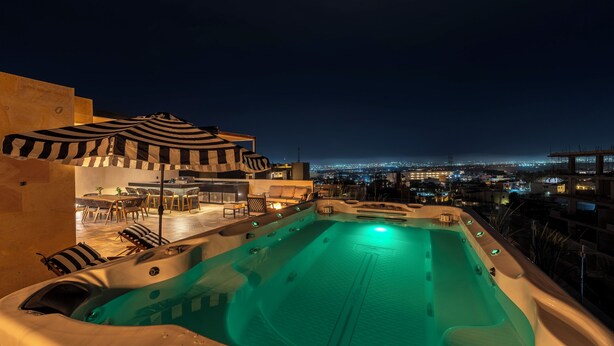 Uma área de piscina no terraço com hidromassagem, espreguiçadeiras e um guarda-sol.