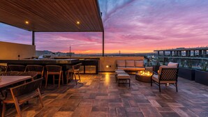 Um terraço ao ar livre com teto de madeira, área de jantar com cadeiras e mesa, um sofá e uma lareira.