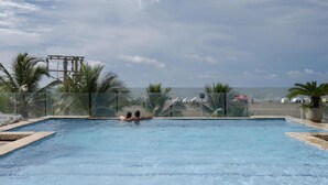 Ein Pool mit Blick auf den Strand, umgeben von Palmen und einem Zaun.