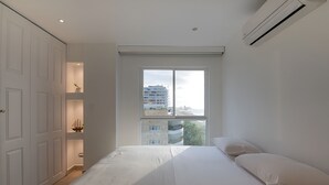 Ein Schlafzimmer mit einem großen Bett, einem Fenster mit Blick auf die Stadt und einem weißen Kleiderschrank.