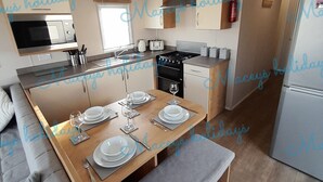 A modern kitchen with a central island, dining table set for four, and a sofa in the adjacent living area. - Pet Friendly Caravan in Walton on the Naze (Walton on the Naze)