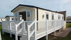 A mobile home with a white exterior, a porch with white railings, and a sliding door. - Pet Friendly Caravan in Walton on the Naze (Walton on the Naze)